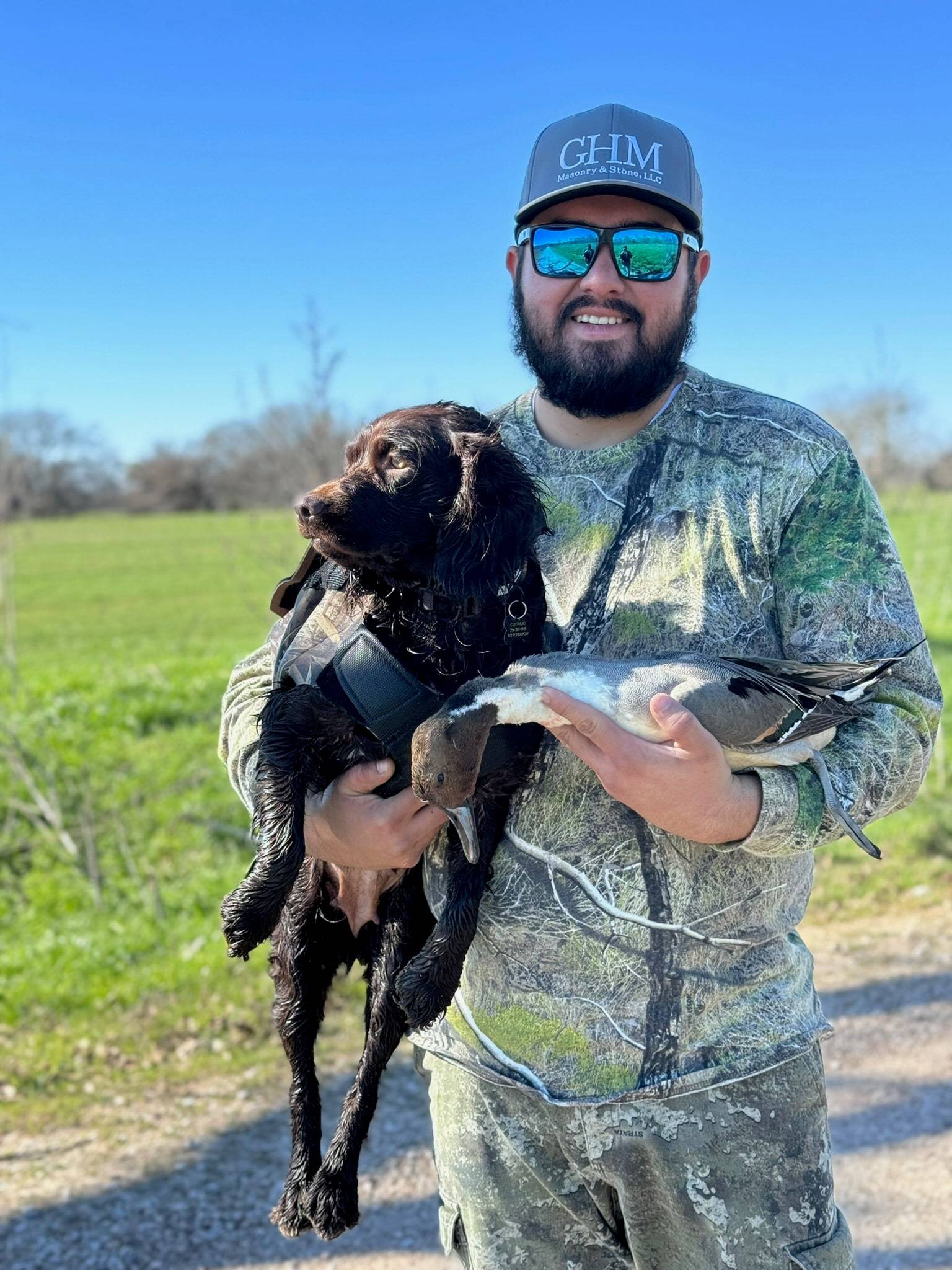 Smiling hunter in camo holding a wet brown spaniel and a drake pintail